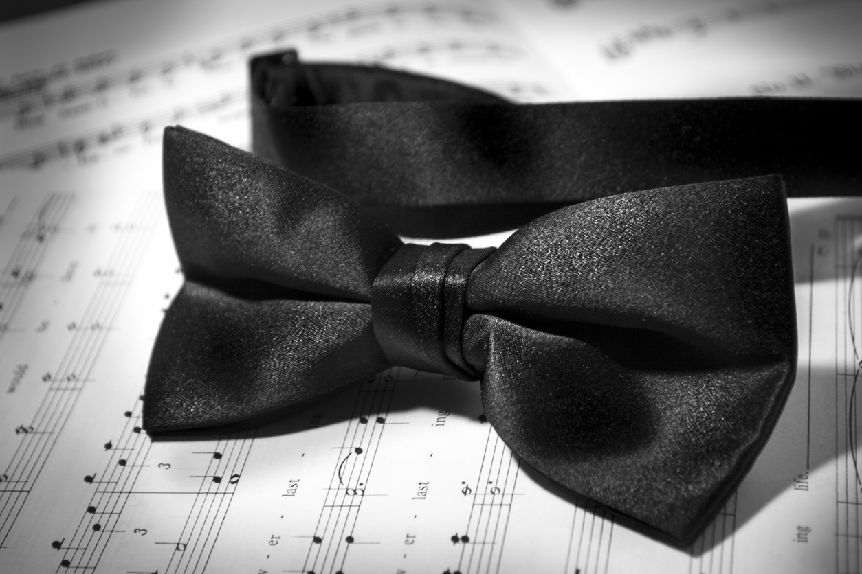 A black bowtie lies upon a musical arrangement