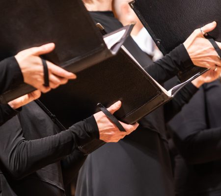 Detail of human hands holding sheet music while singing in choir