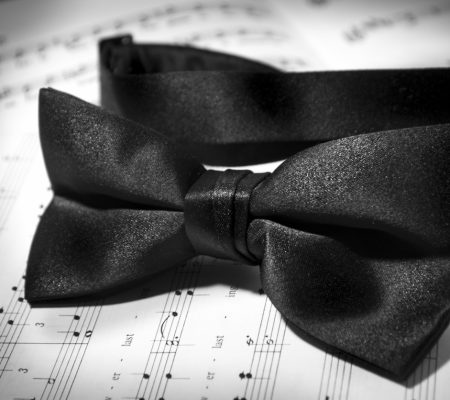 A black bowtie lies upon a musical arrangement