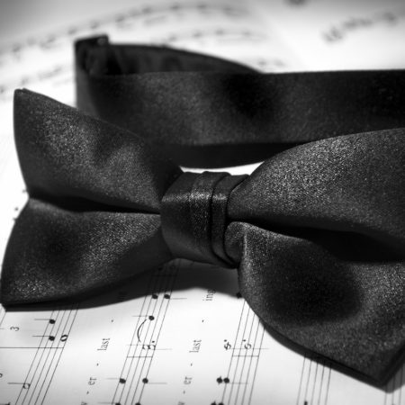 A black bowtie lies upon a musical arrangement